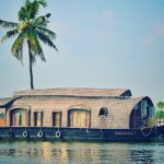 Picturesque view of river with green palms on bank and shabby wooden boathouse under blue sky in tropical countryside